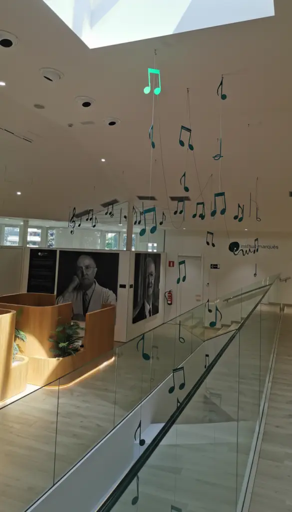 Heller Innenbereich der Kinderwunschklinik Institut Marquès in Barcelona mit hängender Musiknoten-Installation, Glasgeländer und großem Oberlicht.